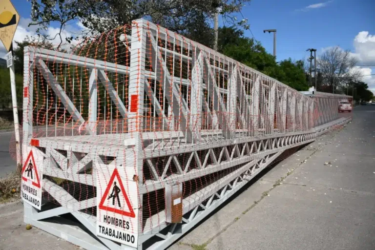 Obreros trabajando en la instalación de un puente peatonal metálico en una avenida.