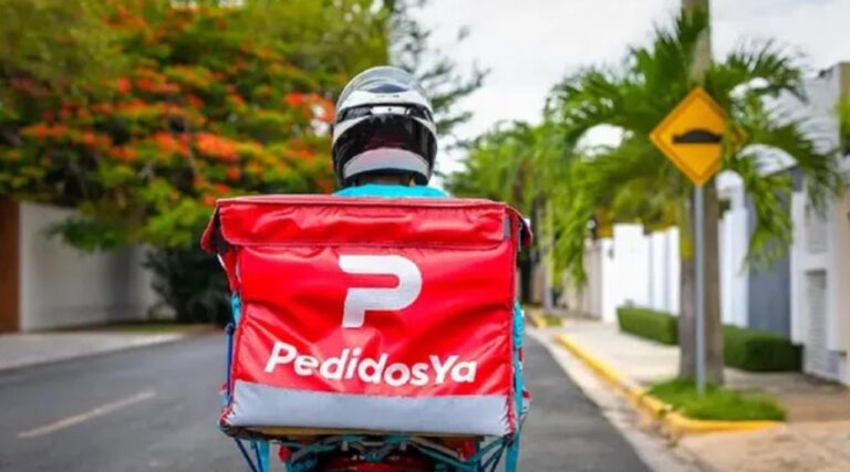 Persona utilizando una aplicación de delivery en su teléfono móvil, con una moto de reparto de fondo.