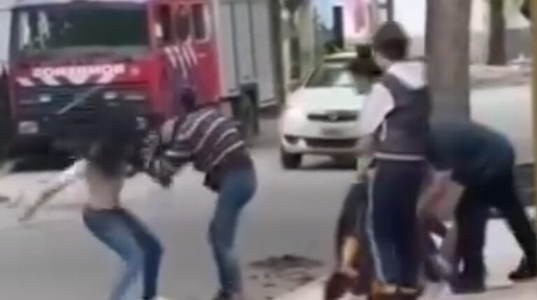 Dos mujeres discuten en una calle céntrica de Metán, con edificios y transeúntes al fondo.